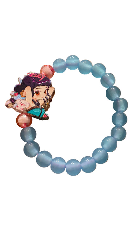 Blue beaded bracelet with a character charm held in a hand against a blurred background